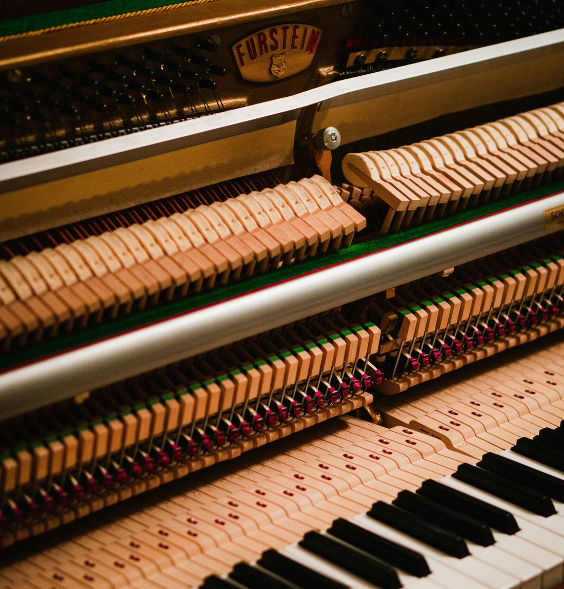 A piano technician's hands at work on the tuning pins inside an open upright piano